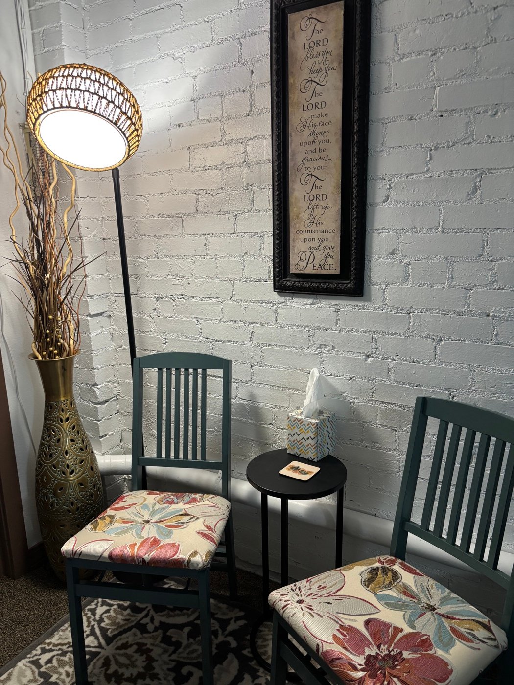 A quiet corner of the studio with chairs, a lamp, and scripture on the wall